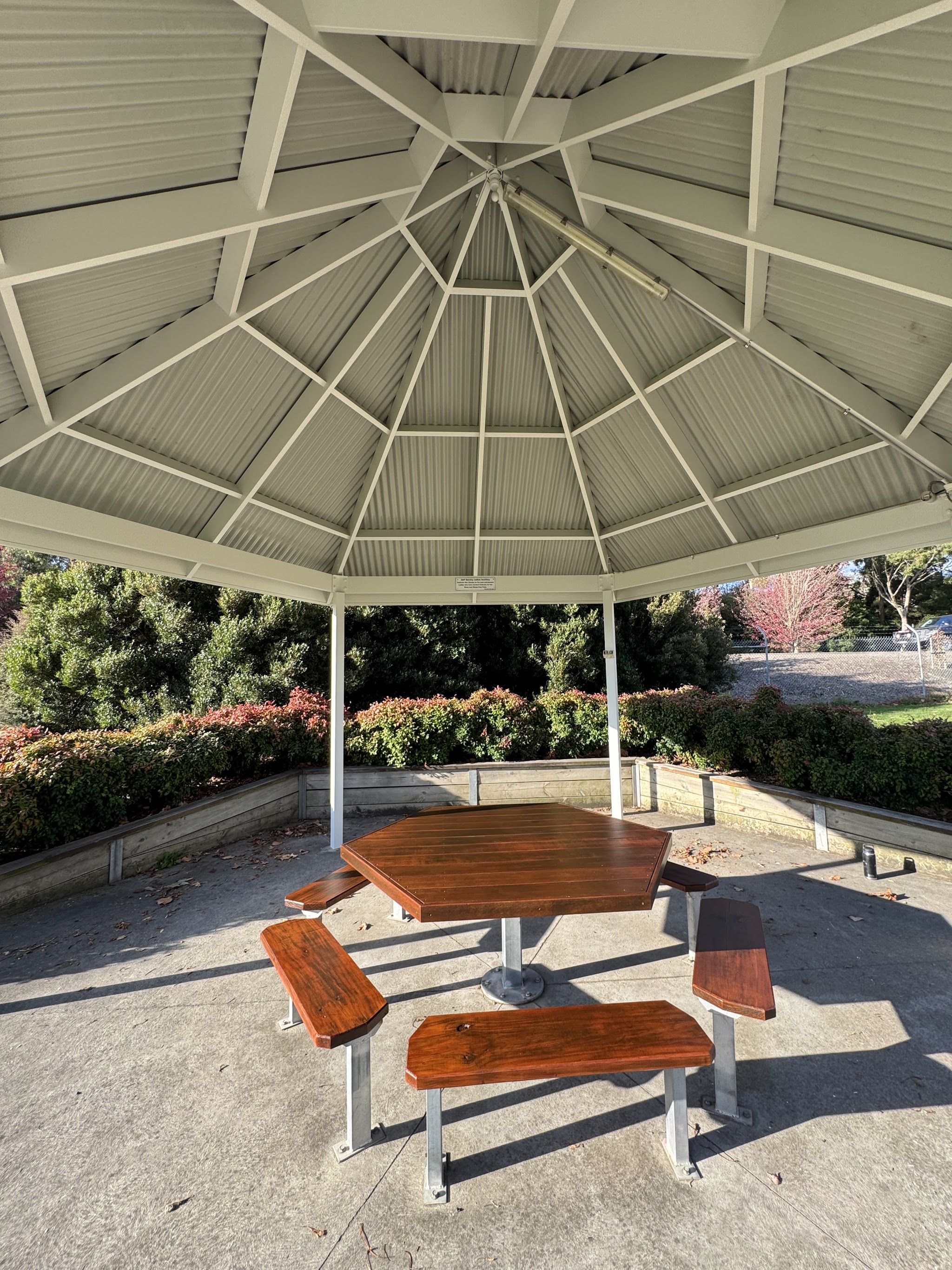 A freshly painted garden rotunda with a stained hexagonal timber table underneath